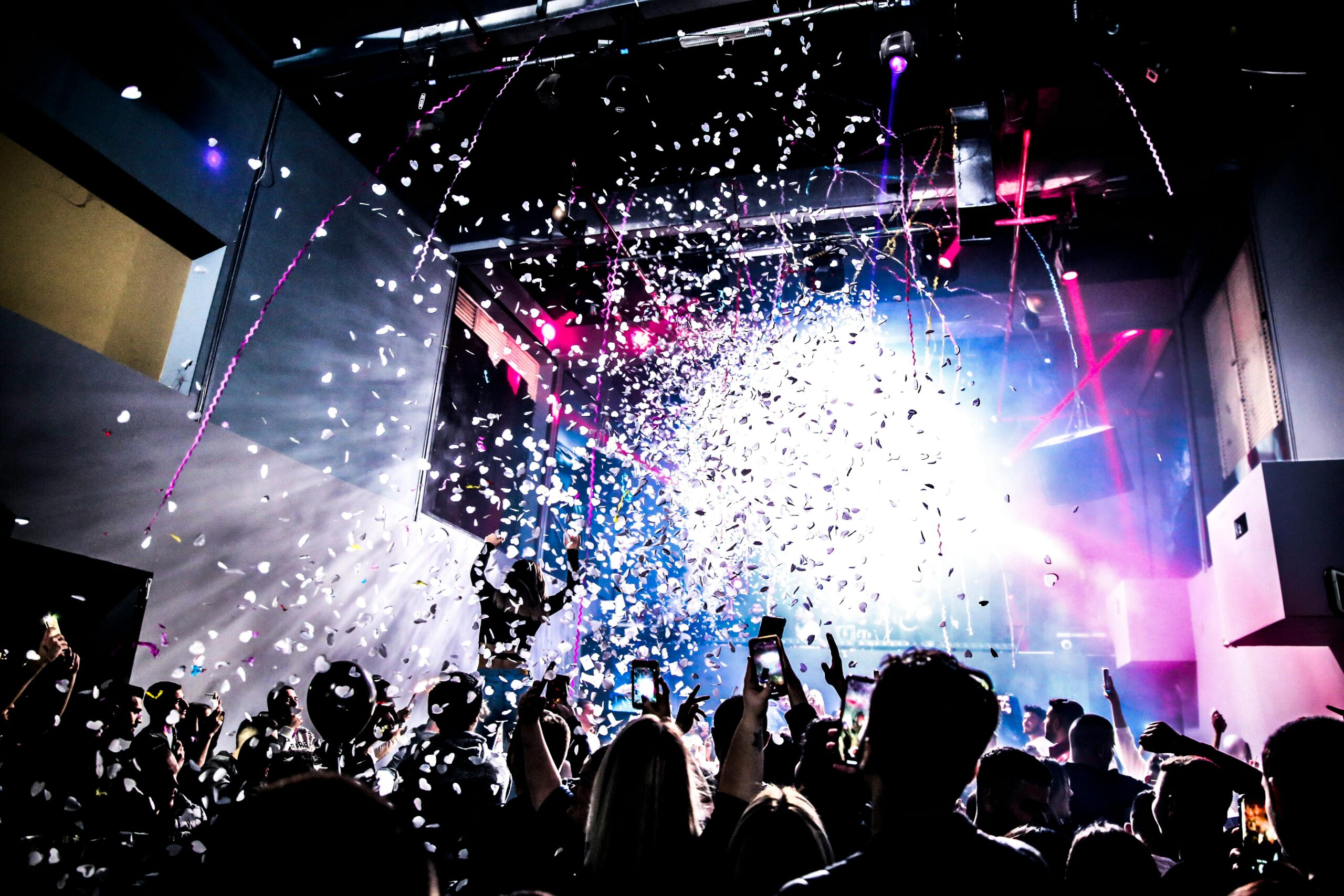 Energetic nightclub scene with crowd dancing under confetti and colorful lights.
